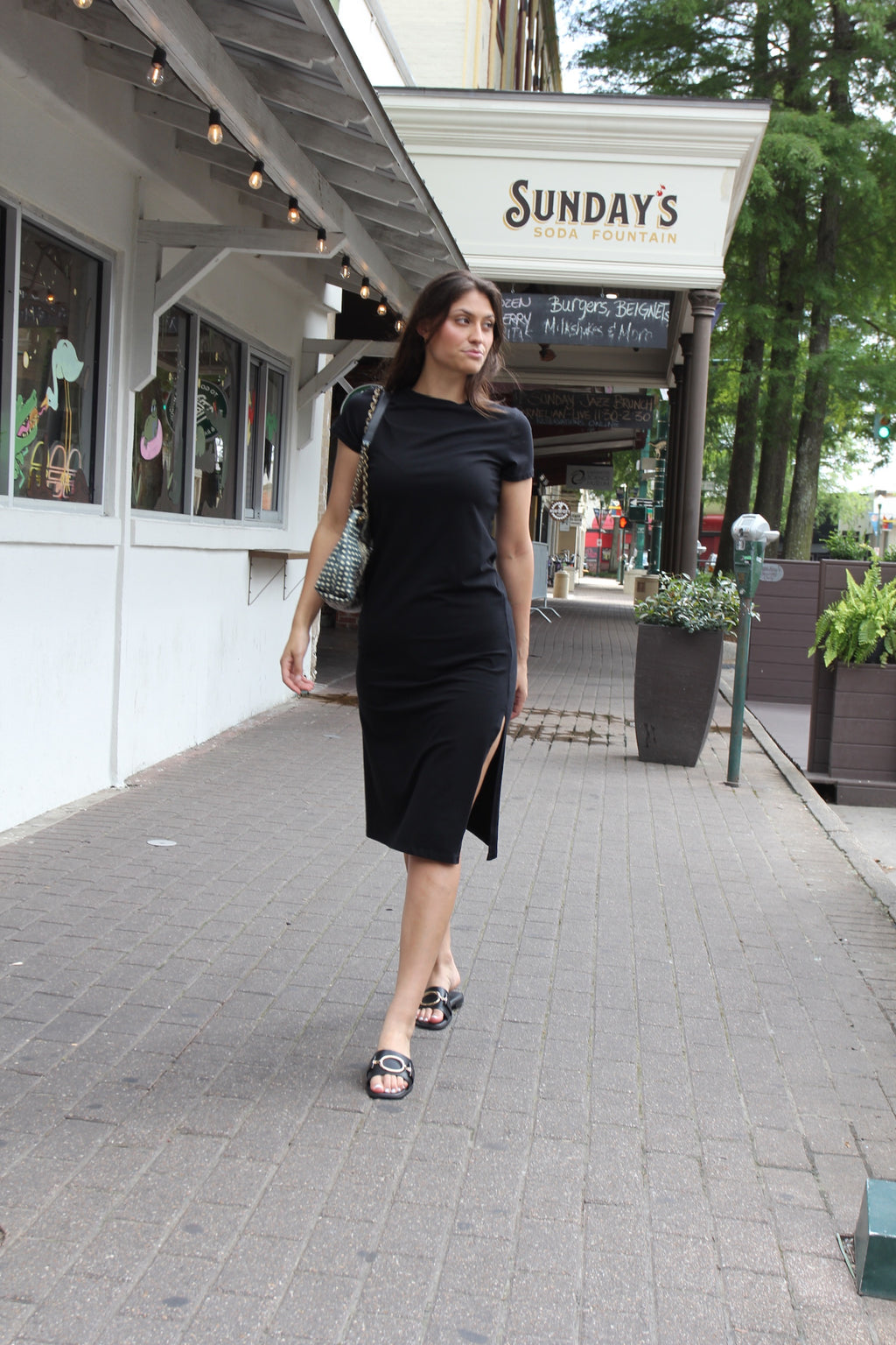 Model wearing fitted black Melissa Nepton midi dress with side slit and short sleeves styled as a minimalist everyday luxury outfit