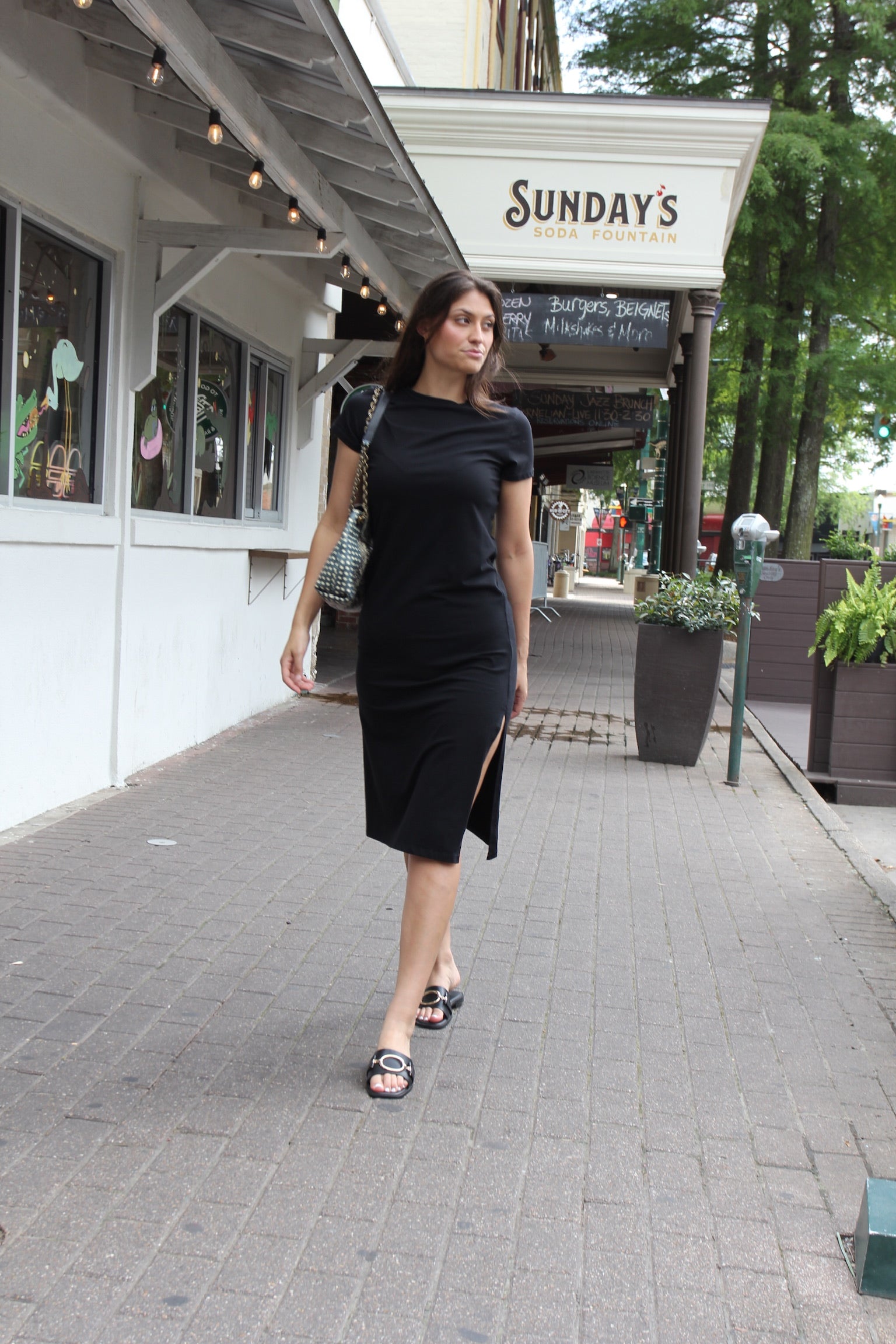 Model wearing fitted black Melissa Nepton midi dress with side slit and short sleeves styled as a minimalist everyday luxury outfit