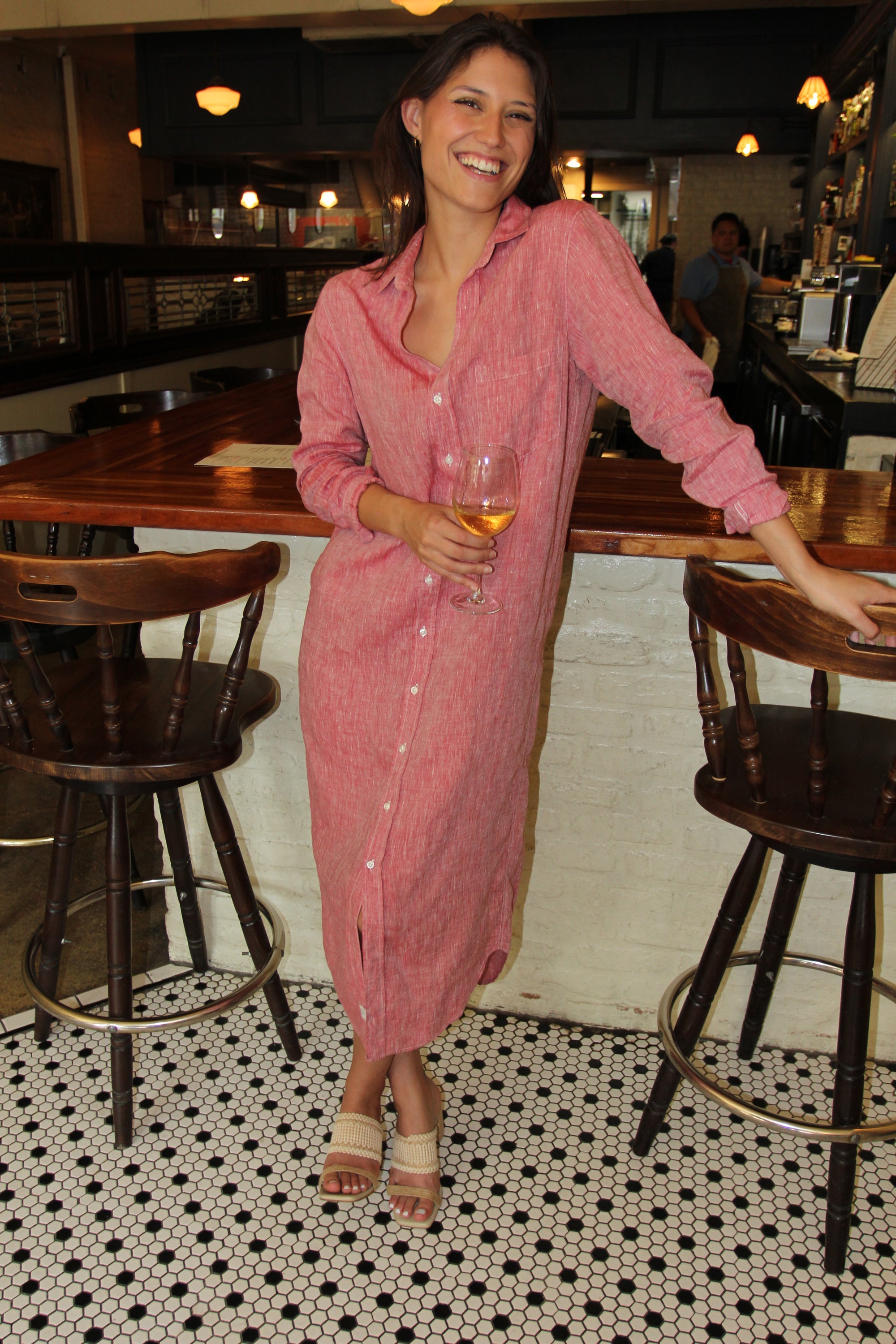 Woman in a pink Italian linen dress standing in a bar with a glass of wine